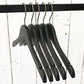 Image of five Rustic Motifs Wooden Antique finish Top 38cm hangers hanging on a black metal rod. The background consists of white wooden panels with visible grain and slight imperfections, giving a vintage feel. The hangers, with an antique finish, are empty and lined up closely together.