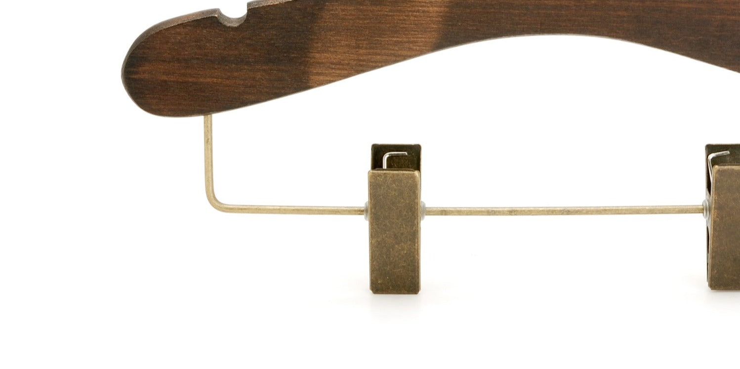 Close-up image of a Rustic Motifs Wooden Antique Kids Top Clip (Brass Hook) 28cm made from dark ash wood with metal clips. The hanger features a dark brown finish and a curved design at the top, with metal clasps attached to the bottom for securing garments. The background is plain and white.