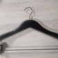 A Wooden Jacket Black With Clips (Black Hook) 39cm by Rustic Motifs with a triangular shape and shoulder notches lies flat on a wooden surface. This stylish display includes adjustable pants clips on the bottom bar, designed for hanging jacket and trousers securely.
