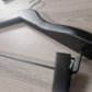 A Rustic Motifs Wooden Jacket Black With Clips (Black Hook) 39cm is lying on a wooden surface. The light wood grain texture enhances the stylish display. The photo, taken at an angle from above, focuses on the top end and bar clip of the hanger.