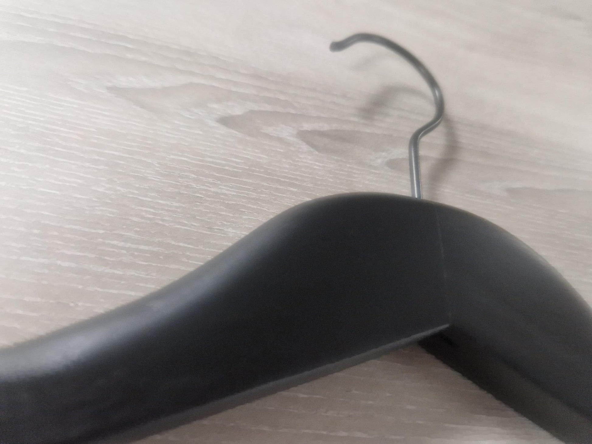 Close-up of a Rustic Motifs Wooden Black Jacket 39cm with a curved hook on a wooden surface. The hanger's smooth and curved design is clearly visible, and the wood grain of the surface adds texture to the background, making it perfect for an elegant jacket display.