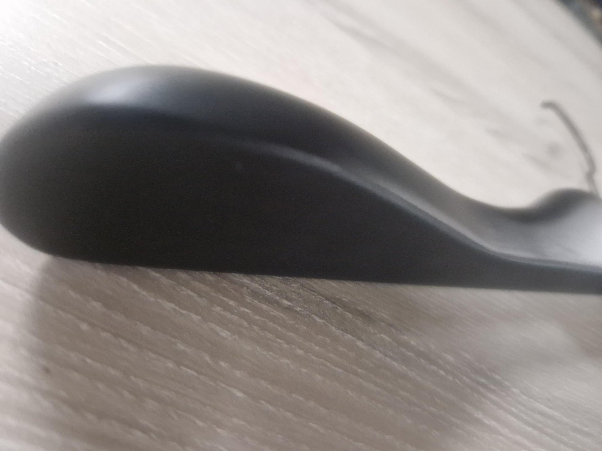 Close-up of a Rustic Motifs Wooden Black Jacket 39cm with a curving shape, resting on a light wood surface. A chunky hanger subtly sits beneath it, blending into the scene. The background is slightly blurred, making it difficult to identify the specific object.