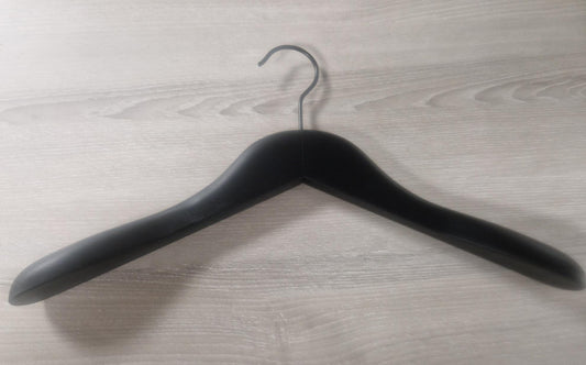 A Rustic Motifs Wooden Black Jacket 39cm with broad, rounded ends and a metal hook lies flat on a light wooden surface. The hanger's design is simple and functional, intended to prevent clothes from slipping off.