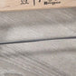 A close-up image of an untreated Wooden Natural Clip Branded Penguin 35cm with metal clips designed to hold pants or skirts. The hanger features the brand name "Rustic Motifs" printed on it, and the background is a textured gray surface.