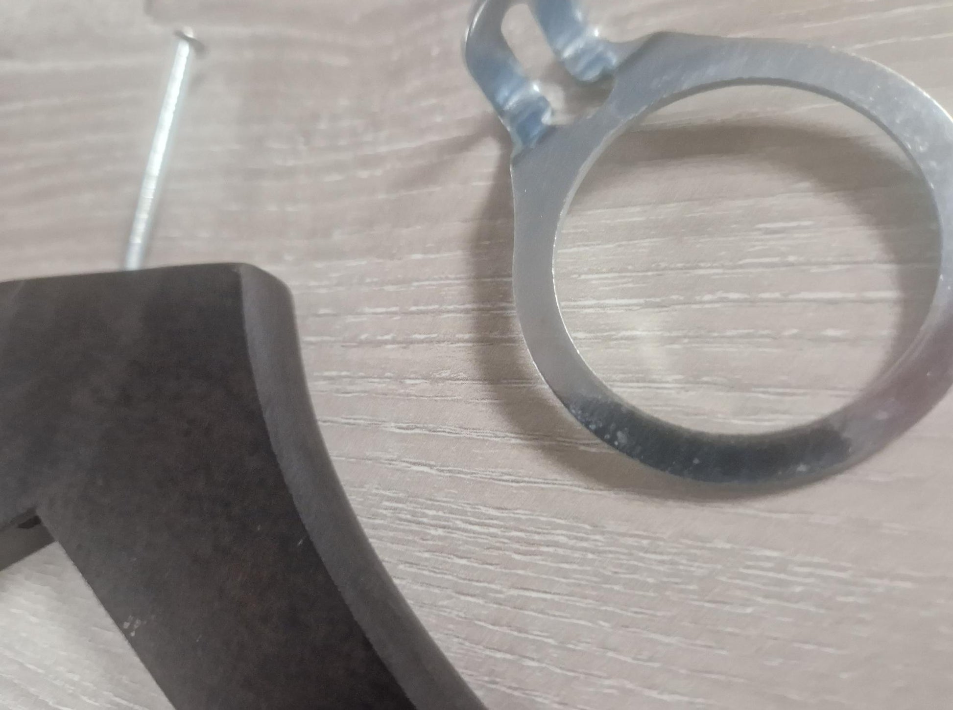 Close-up of a **Rustic Motifs Wooden Hotel Anti Theft Jacket (Dark Brown) 44cm** with a protruding screw on a wooden surface, accompanied by a round metal washer with tabs in a dark brown finish. The image focuses on the hardware components, suggesting construction or assembly work.