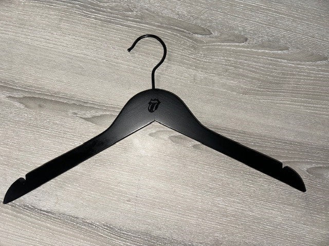 A Black Wooden top hanger branded Rolling Stones 38cm by Rustic Motifs, featuring their iconic tongue and lips design, sits on a gray wooden surface. Perfect for dresses or strapped shirts, this hanger comes in a pack of 50.