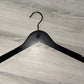 A Black Wooden top hanger branded Rolling Stones 38cm by Rustic Motifs, featuring their iconic tongue and lips design, sits on a gray wooden surface. Perfect for dresses or strapped shirts, this hanger comes in a pack of 50.
