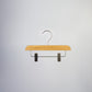 A Rustic Motifs Bamboo Wood Sustainable Clip Bottom Hanger 26cm with a metal hook and two metal clips is suspended against a neutral gray background. The eco-friendly hanger appears simple and sturdy, suitable for hanging pants or skirts.