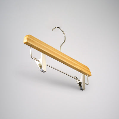 A Bamboo Wood Sustainable Clip Bottom Hanger 35cm by Rustic Motifs with a metal hook and adjustable clips for securing clothing. The hanger is set against a plain gray background, showcasing its simple and functional design as an eco-friendly wardrobe accessory.