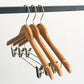 Three Rustic Motifs Bamboo Wood Sustainable Top Clip Hanger 42cm with metal hooks hang on a black metal rod. The eco-friendly clothing organizers also feature metal clips for securing garments. The background is plain white.