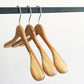 Three Rustic Motifs Bamboo Wood Sustainable Top Jacket Hanger 42cm are hanging on a black metal rod against a white background. The hangers are evenly spaced and have a smooth, polished finish.