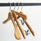 Three Rustic Motifs Bamboo Wood Sustainable Top Clip Hanger 42cm are hanging on a black metal rod. Two of the eco-friendly clothing organizers have a standard shape, while one includes metal clips for holding pants or skirts. The background is plain white.