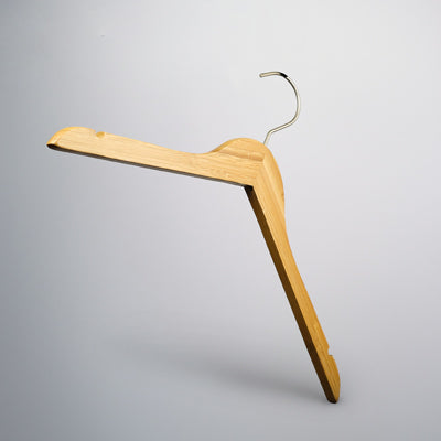 A Rustic Motifs Bamboo Wood Sustainable Top Hanger with Notch 42cm, featuring a silver metal hook, is suspended against a light grey background. The hanger has notches on both ends, ideal for securing straps of clothing. The design is simple and functional.