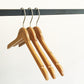 Three Rustic Motifs Bamboo Wood Sustainable Top Hangers with Notch 42cm hang on a black metal rail against a plain white background. The hangers are evenly spaced and aligned, with their metal hooks visible at the top, creating a simple and minimalist composition.
