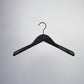 A single, Rustic Motifs Black Wooden Jacket Top Coat Hanger 38cm is suspended against a plain, light gray background. This high-quality hanger features broad, slightly curved shoulders and a metal hook at the top.