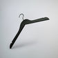 A Black Wooden Top Clothes Hanger with Notch 44cm by Rustic Motifs is suspended against a minimalist, light gray background. This top-notch clothing storage solution features a standard hook at the top and angled arms with shoulder notches for securing garments.