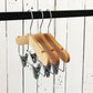 Three Rustic Motifs Natural Wood Coat Kids Hanger with Bar 28cm are hanging on a black rod against a white wooden plank wall. These high-quality hangers are evenly spaced and aligned in a row, ideal for organizing a child's wardrobe.