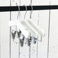 A set of three White Wood Top Coat Kids Hanger with Bar 28cm, known as Rustic Motifs, hangs on a black clothing rod. The background features a white wooden panel wall with visible grain and rustic texture.