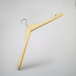 A high-quality wood hanger with a metal hook is suspended against a plain, light grey background. The Rustic Motifs Natural Wood Top Clothes Hanger with Notch 38cm features a notch on each end and a slight, curved shape.