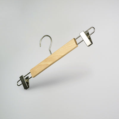 A Rustic Motifs Natural Wooden Clip Bottom Hanger 37cm, crafted from sustainable solid wood and featuring durable metal clips and a hook, is suspended against a plain, light-colored background.