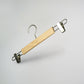A Rustic Motifs Natural Wooden Clip Bottom Hanger 37cm, crafted from sustainable solid wood and featuring durable metal clips and a hook, is suspended against a plain, light-colored background.
