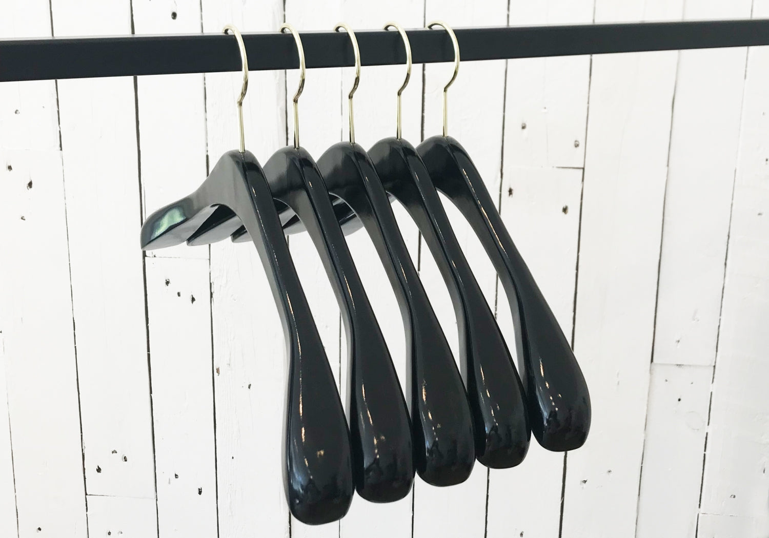 Five high-quality black wood hangers are hanging on a silver metal rod against a white wooden wall. The Rustic Motifs Black Wooden Top Coat Premium Hanger 42cm are evenly spaced, and the setting appears minimalist. The nonslip grip ensures your clothes stay securely in place.