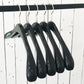 Five high-quality black wood hangers are hanging on a silver metal rod against a white wooden wall. The Rustic Motifs Black Wooden Top Coat Premium Hanger 42cm are evenly spaced, and the setting appears minimalist. The nonslip grip ensures your clothes stay securely in place.