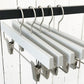 A row of Rustic Motifs Premium Soft Touch Plastic Clip Hanger 35cm with metal clips and hooks hangs on a black metal rod. The background features a white wooden plank wall, showcasing stylish storage solutions for any wardrobe.