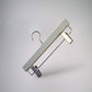 A minimalist white, Rustic Motifs Premium Soft Touch Plastic Clip Hanger 35cm with a metal hook and two silver clips, suspended against a plain gray background. The clips are positioned on the bottom bar of the hanger, designed to hold pants or skirts – a stylish storage solution for any wardrobe.