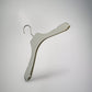 A single beige Rustic Motifs Premium Soft Touch Plastic Coat Hanger 39cm with a metal hook is suspended in front of a neutral gray background. The elegant hanger features a curved design to accommodate the shape of garments, perfect for enhancing closet organization.