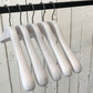 Five premium-quality White Ash Wooden Jacket Coat Hanger 44cm by Rustic Motifs are hanging on a black metal rod against a background of white wooden planks.