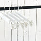 A row of Rustic Motifs White Wooden Clip Bottom Hanger 37cm is hanging on a black rod. The backdrop is a rustic white wooden wall with visible nails and cracks, providing the perfect setting for crease-free garment organization.